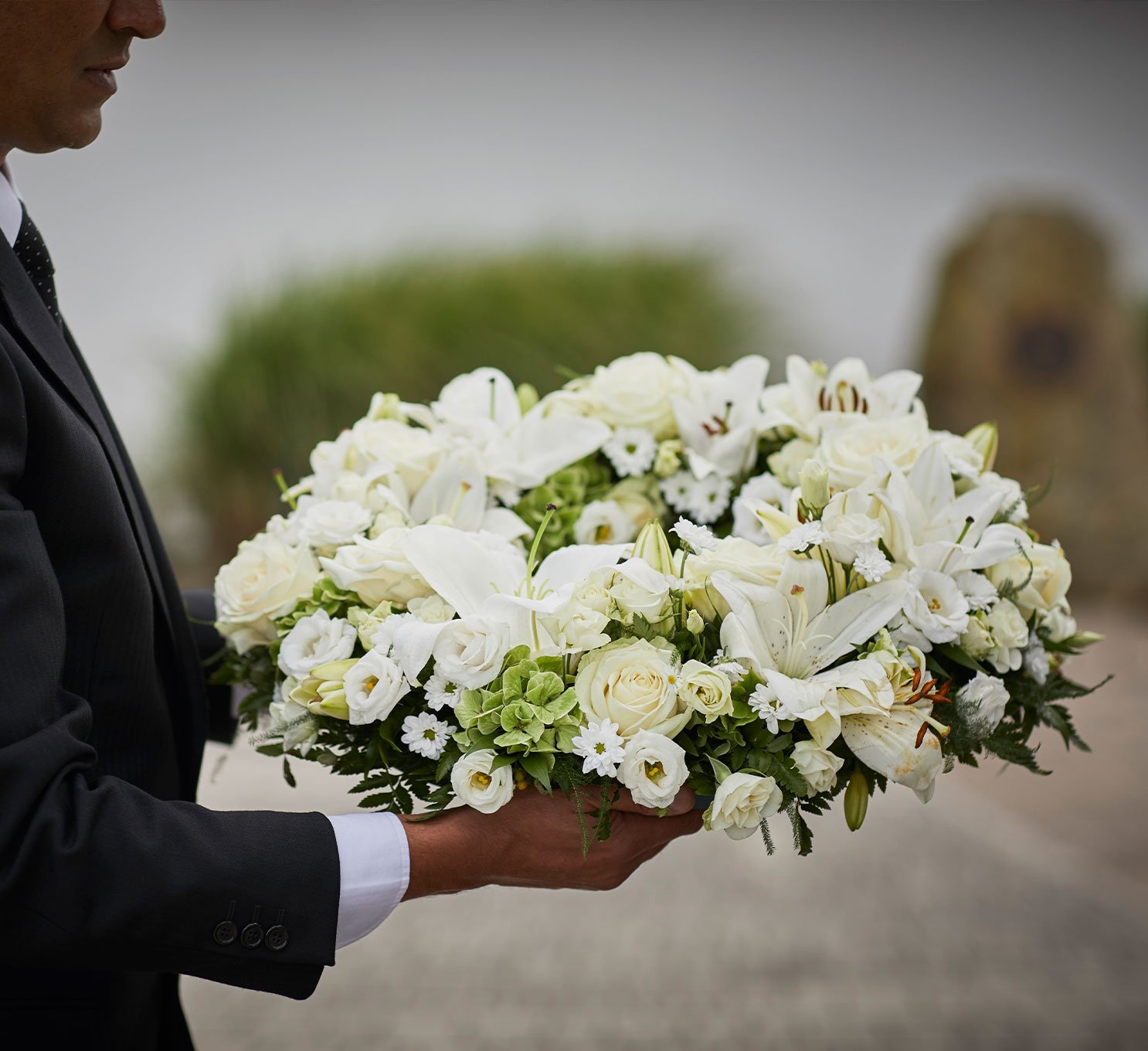 A funeral directors carries a wreath of white flowers