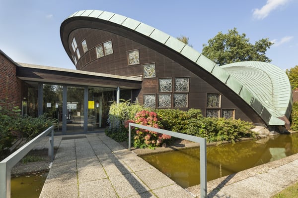 Eingangsbereich des Kirchengebäudes. Das Gebäude und das Dach zeichnen sich durch Schrägen und Rundungen aus.