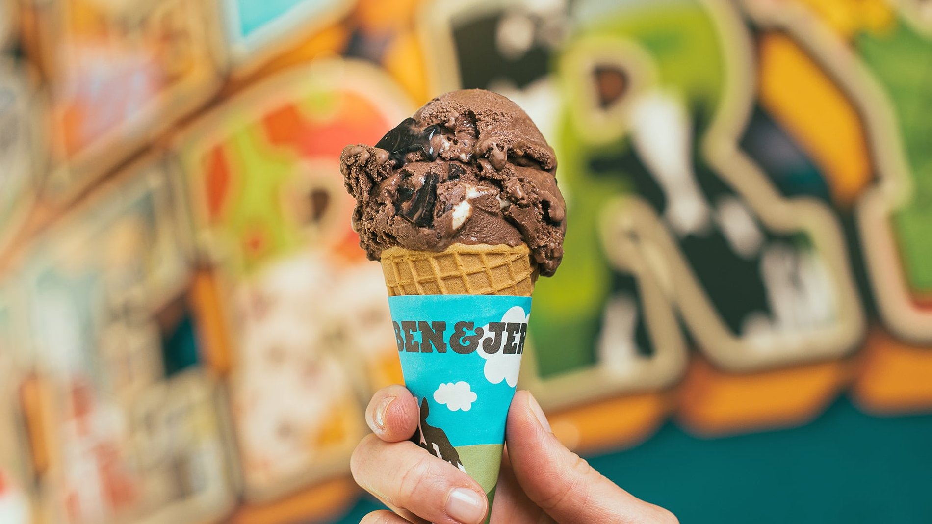 A hand holds up Ben & Jerry's Rocky Road Ice cream in a Waffle Cone.
