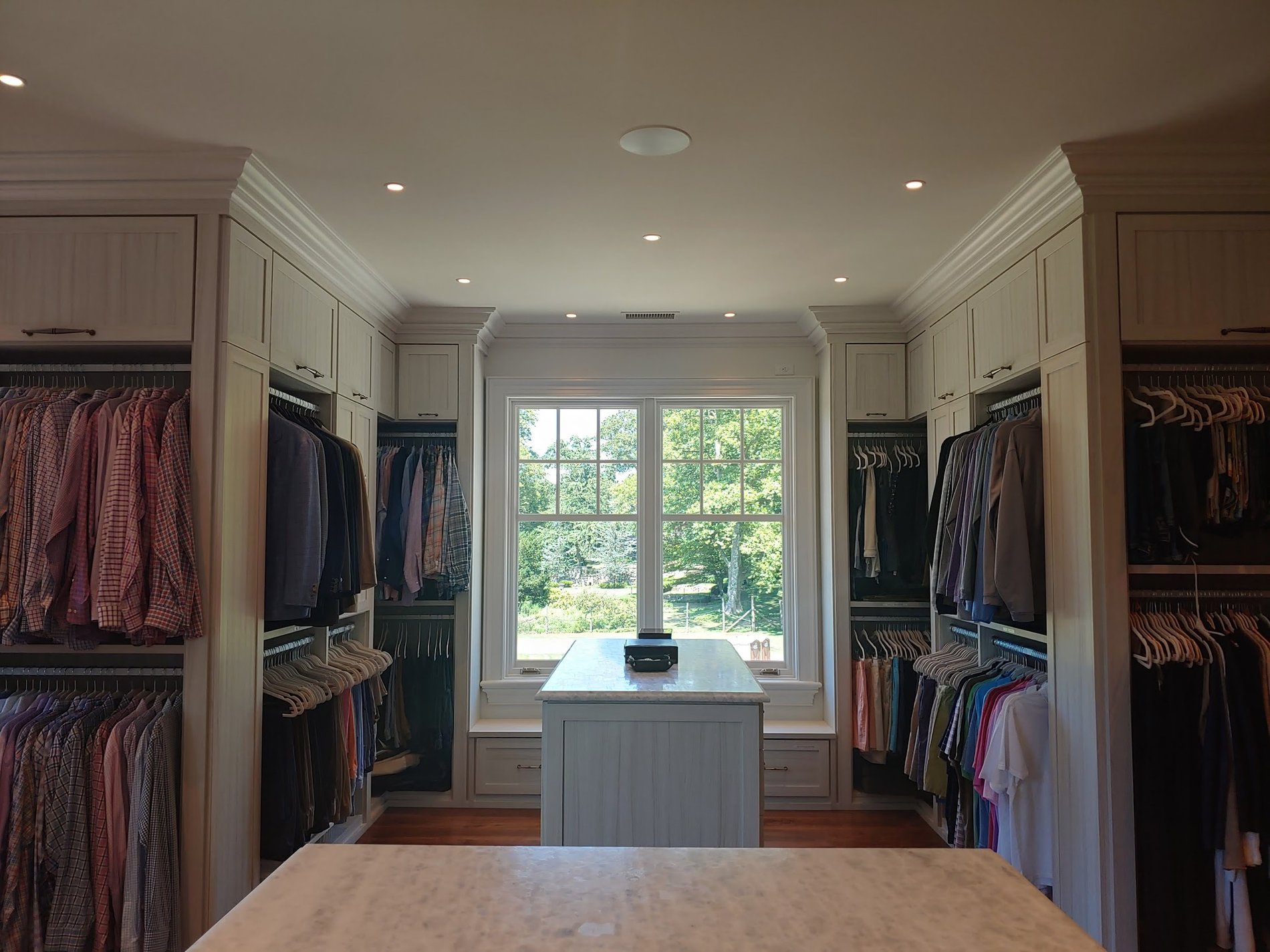 Large walk-in closet with hanging clothes, island and window