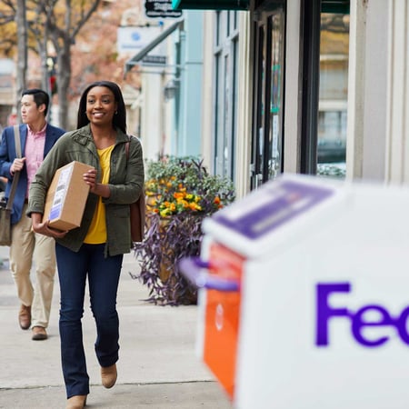 a person holding a box and walking towards a FedEx Drop Box