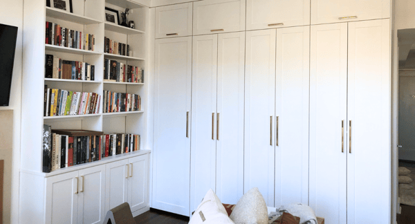 white custom living room unit, one side open bookshelving with closed cabinetry adjacent, floor to ceiling shaker doors with gold metal hardware for door handles Manhattan New York City