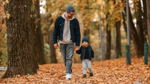 Man and young child walking on leaves.