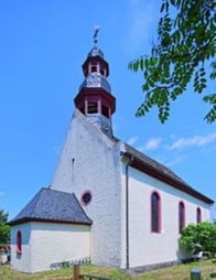 Außenansicht St. Martinskirche Wackernheim. Die Großteil der Kirche ist weiß gehalten, während das Dach schwarz mit roten Akzenten gefärbt ist.