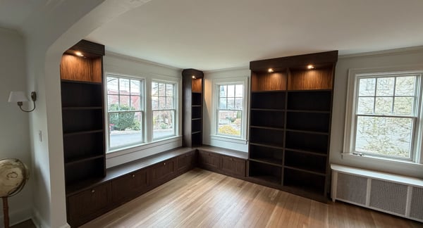 Dark wood built-in home library with window seats and storage underneath.