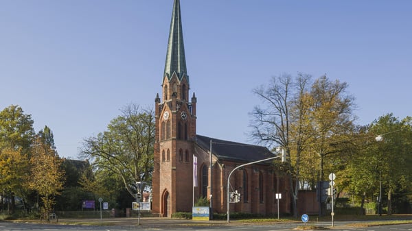 Kirchengebäude an einer Straßenkreuzung, von Bäumen umringt.