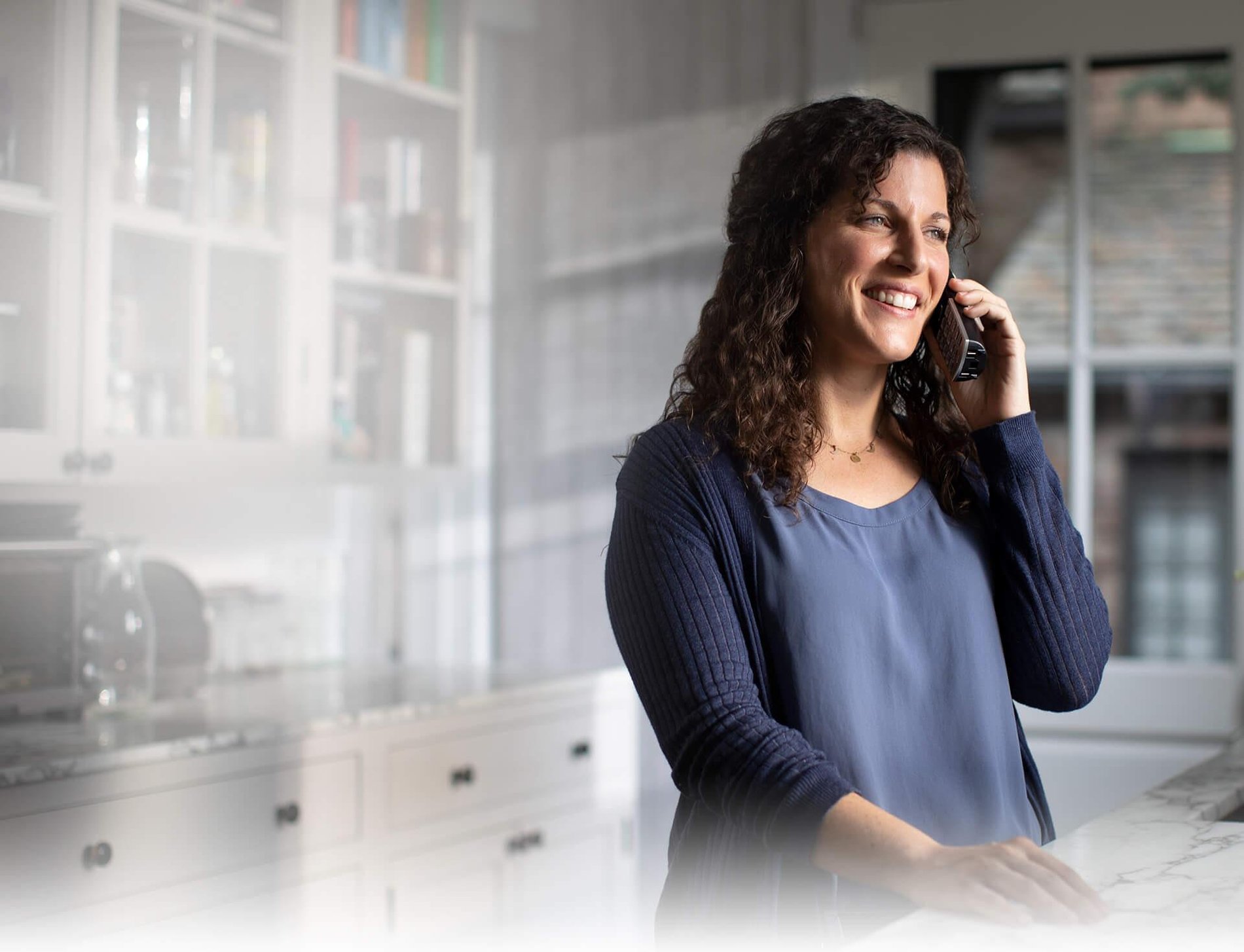 Foto de una mujer parada en la cocina hablando con un teléfono inalámbrico y usando una conexión de Suddenlink Voice