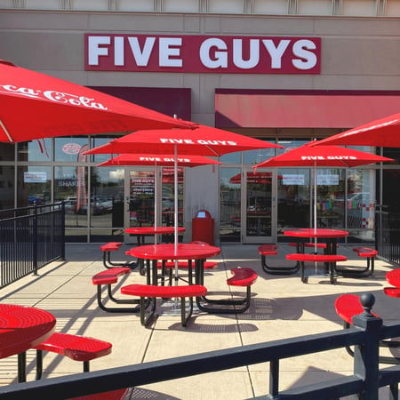 Exterior photograph of the Five Guys restaurant at 6685 Whitestown Parkway in Zionsville, Indiana. The image displays the outdoor seating and umbrellas of the location.