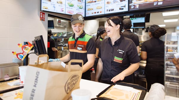 Burger King Employees laugh as they stand behind a counter, packing customer orders.