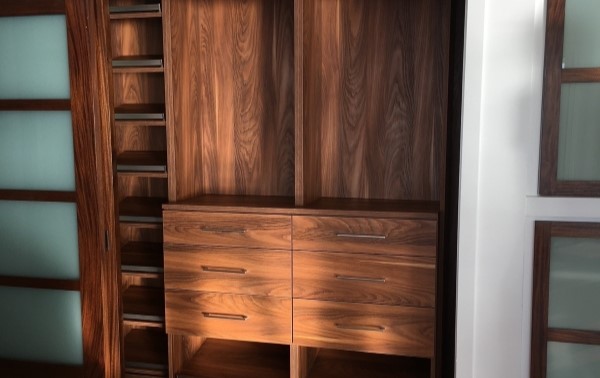Reach-in closet in warm brown finish with drawers, shelving and hanging space with coordinated sliding doors.
