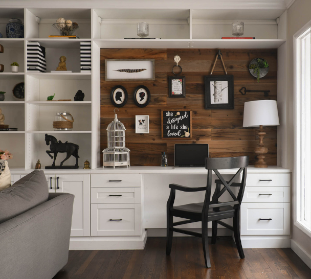 Custom built desk in living room for nook workspace with natural dark wood on the back and white floor-to-ceiling drawers, crown molding, and shelving to display collectibles