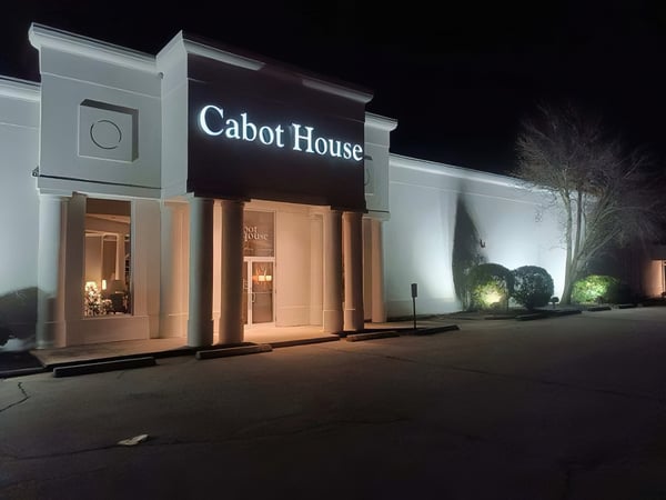Storefront of Cabot House Furniture Waymouth location at night with lit up entryway and landscaping.