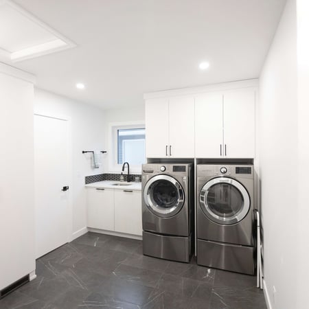 Simple white laundry room. Upper cabinets over the washer and dryer with lower cabinets to the side.