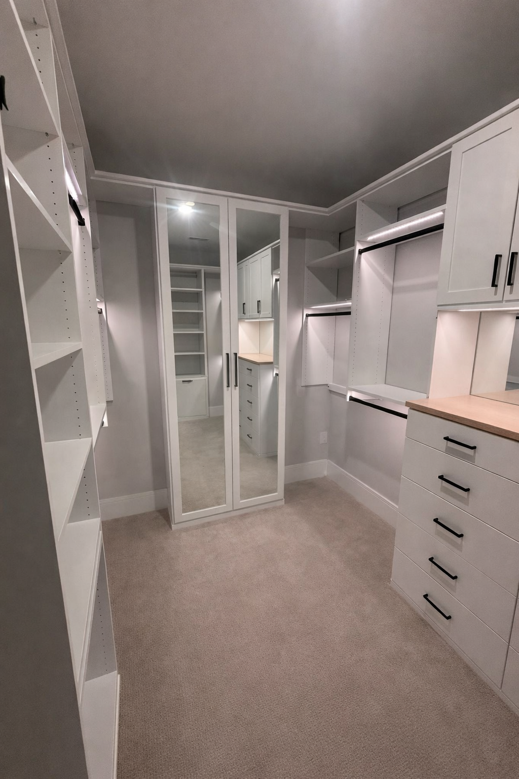 Custom Primary Walk in Closet in Dove with drawers, lighting, hanging, shelving, and doors.