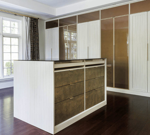 Img 1 - California Closets Beige and Bronze Full Room Dressing Room Walk-in Closet with Glass Bronze Doors Closed Cabinetry and Center Island with Brown Leather Drawer Faces and Clear Bronze Glass Countertop