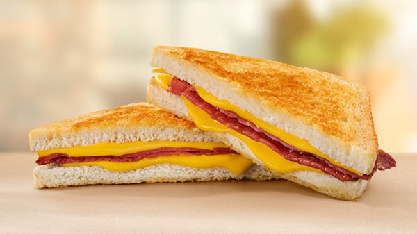 A Macon & Cheese Toasted Sandwich on a brown surface with a blurred background.