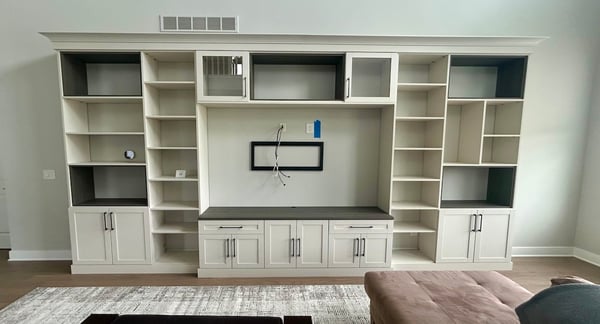 light wood media center with shaker cabinets and open shelving, dark accent shelves, and a centered TV mount