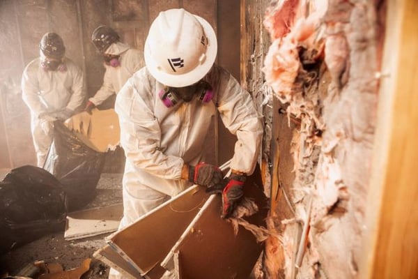Pro in protective wear pulls fire damaged drywall at a site.