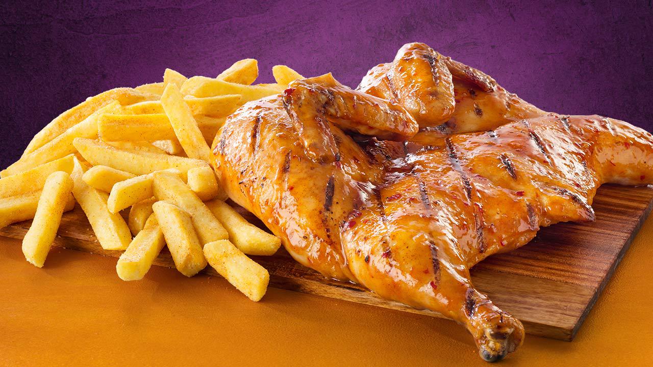 Steers flame-grilled chicken on a wooden table next to a full portion of chips in front of a purple background.