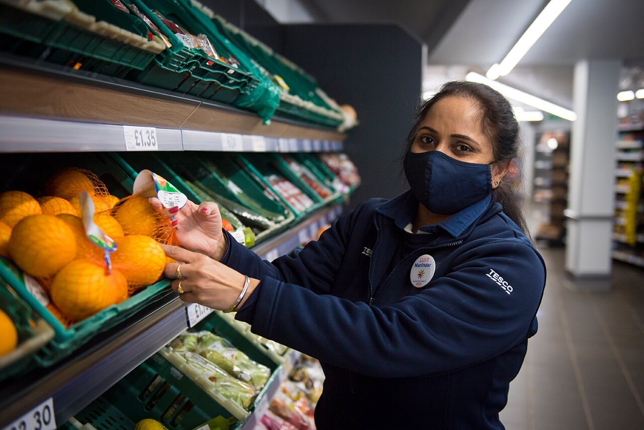 Tesco worker wearing face mask and stocking oranges.