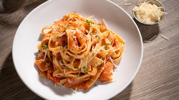 A white bowl with fettuccine pasta with strips of salmon and chopped parsley.