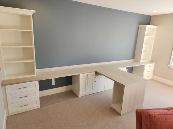 A double desk office space with bookshelves and drawers for storage.