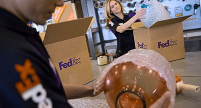 Two FedEx employees packing a glass vase