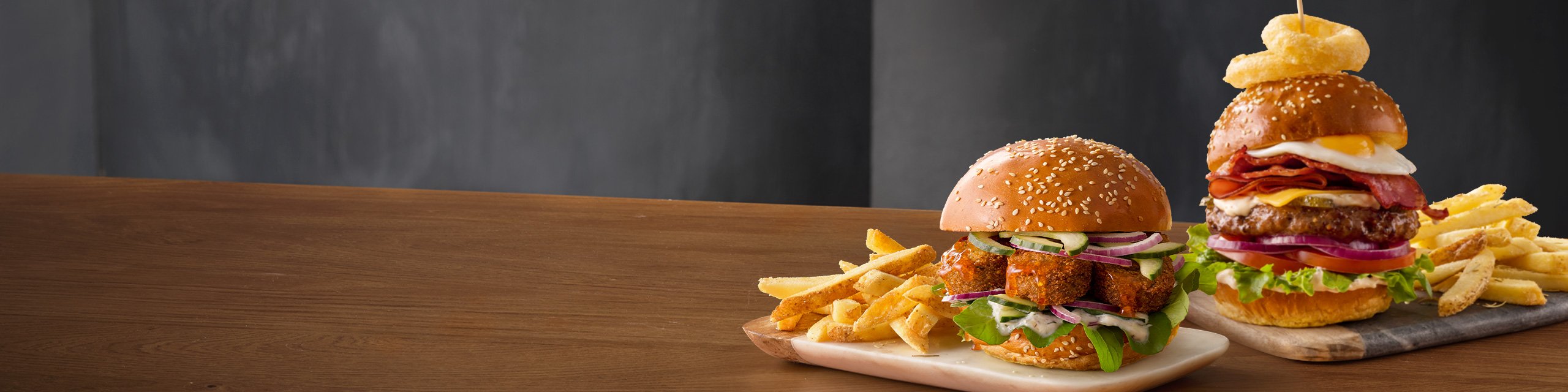 Mugg & Bean Gourmet Burgers – Big Daddy and Buttermilk Chicken with a portion of chips, on a wooden table