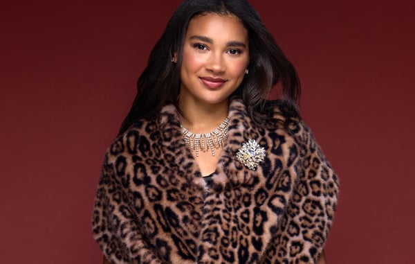 Woman wearing an animal print faux fur coat with statement jewelry, posing in front of a dark red background