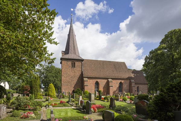 Das Kirchengebäude umgeben von einem Friedhof und Bäumen.
