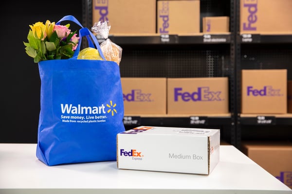 A blue Walmart shopping bag and a FedEx Express Medium Box on a counter, with FedEx shipping supplies in the background.