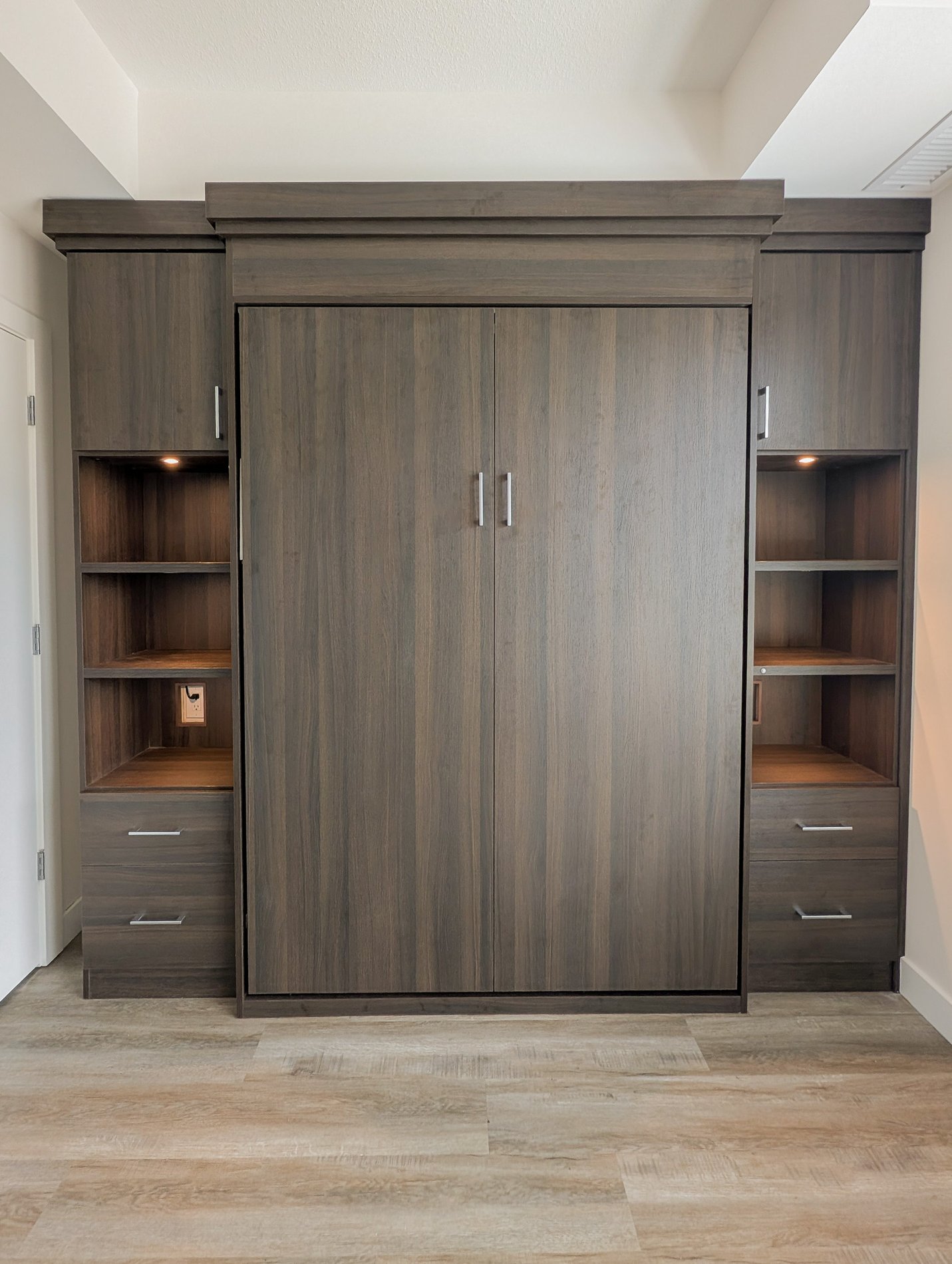 Dark and elevated wall bed with closed storage, opening, shelving, and lighting.