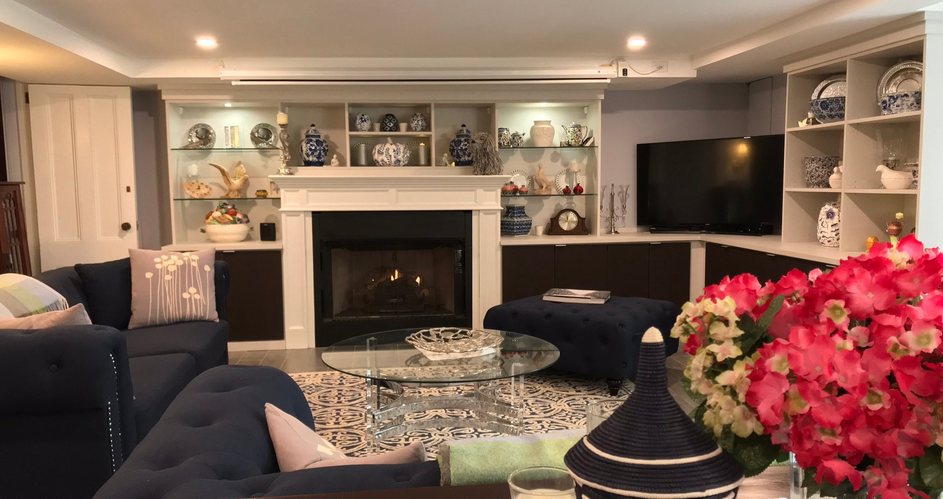 living room with built-in shelves filled with collectables, fireplace and TV, couch and flowers in foreground