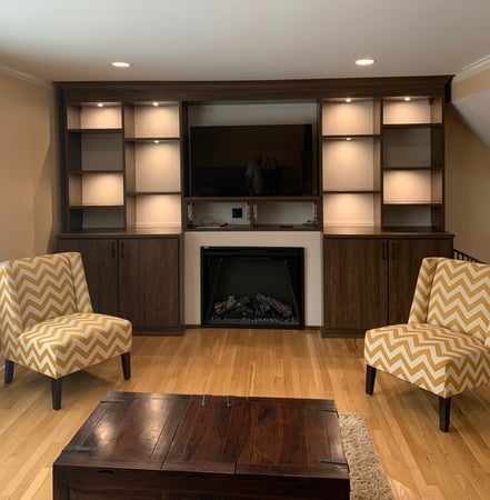 brown built-in shelves with lighting, fireplace and two yellow chairs with coffee table