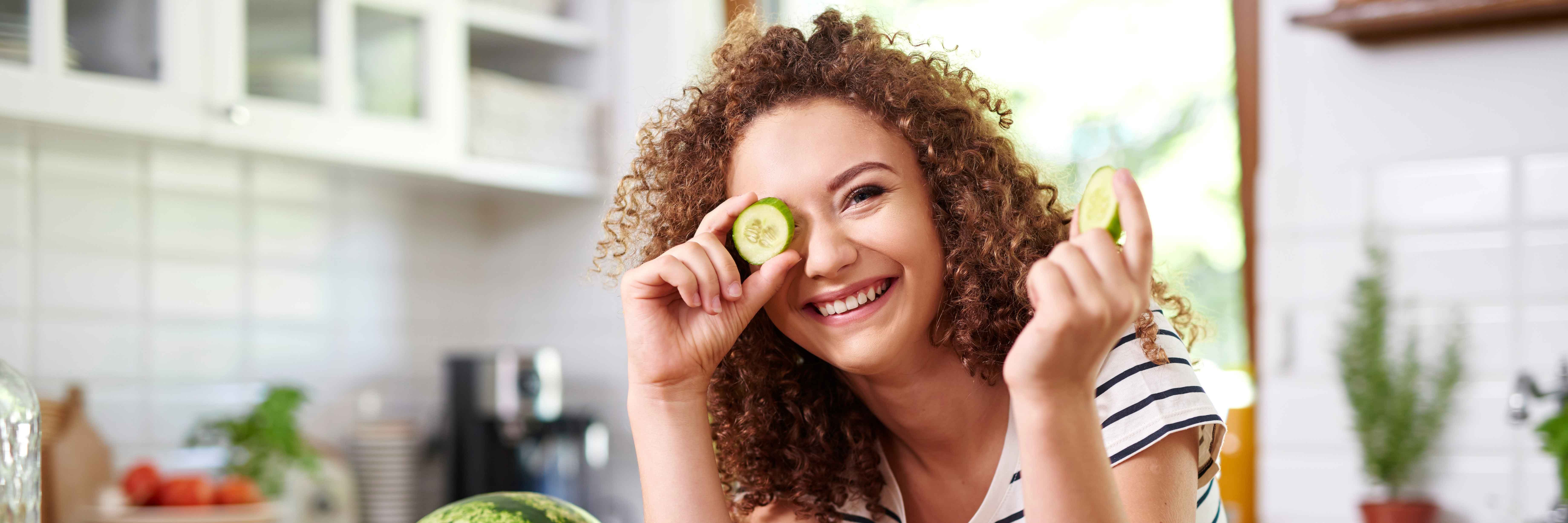 woman holding a cucumber slice up to her eye
