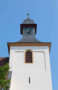 Zu sehen ist der Kirchturm der Kirche Aspisheim vor blauem Himmel.