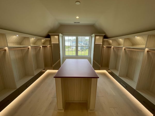 closet with sloped ceiling, hanging space and lighting, center island in light wood color