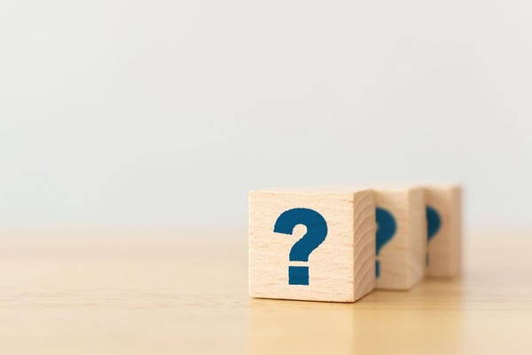 木製のテーブルの上に、疑問符の記号が付いた木製の立方体ブロックの形をした木片が置かれている。