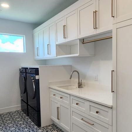 Custom laundry room in Dove finish with gold and brass hardware, featuring smooth knobs and handles, and a Virtuoso suspended round hanging rod.
