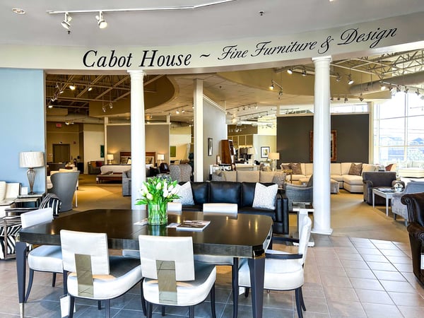 Interior of Saugus location of Cabot House Furniture showing a contemporary dining room set with dark wood table and cream chairs with metallic accents.