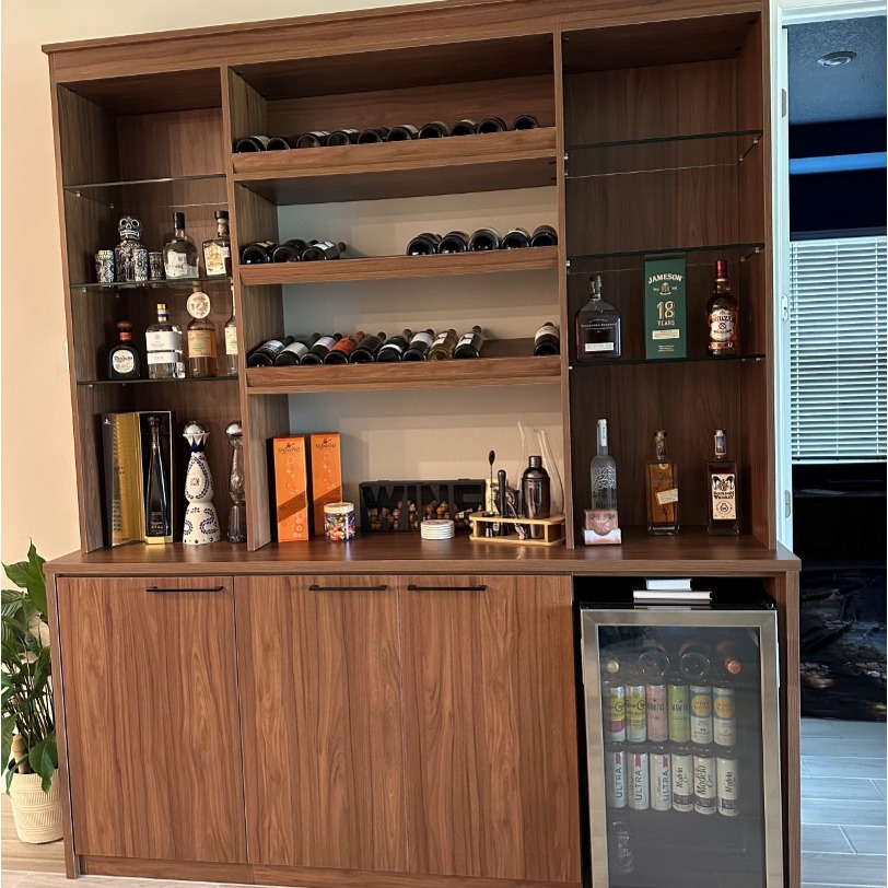 Custom bar in Siena board finish with black hardware, featuring an opening for a wine cooler, angled wine storage shelves, and tempered glass side shelving.