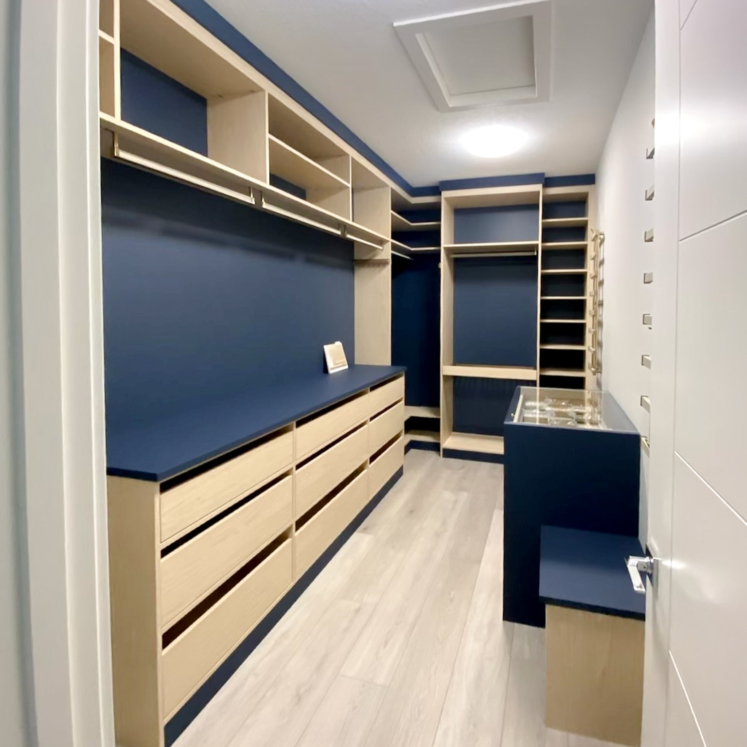 Walk in closet designed in a matte navy blue backing and countertop with natural shelving and drawer fronts.