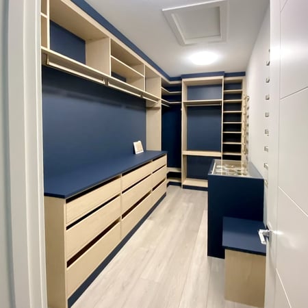 Walk in closet designed in a matte navy blue backing and countertop with natural shelving and drawer fronts.
