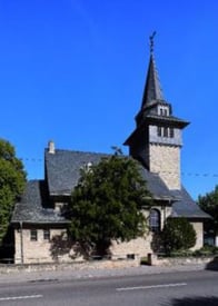 Zu sehen ist ein Kirchengebäude mit Turmspitze vor blauem Himmel.