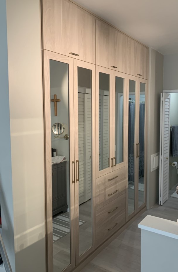 Floor-to-ceiling wardrobe closet in light finish with tall doors with glass inserts.