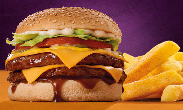 Steers flame-grilled burger on a wooden table next to a full portion of chips in front of a purple background.