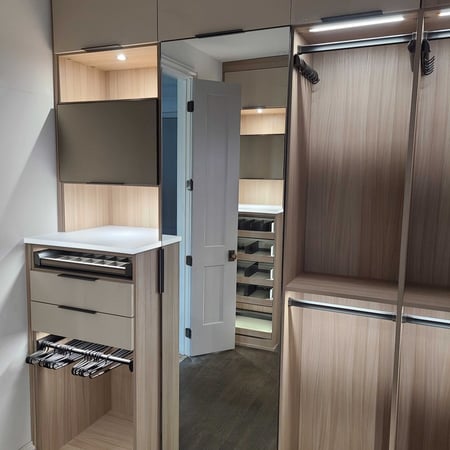 Custom wood walk-in closet with integrated lighting, hanging storage, built-in drawers, shelving, and wardrobe organization.