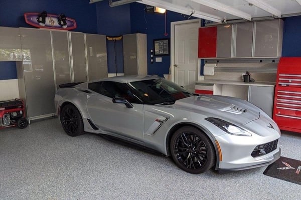 Luxury garage with custom cabinetry, overhead storage, work surfaces, and organized storage surrounding a sports car.