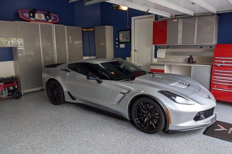 Luxury garage with custom cabinetry, overhead storage, work surfaces, and organized storage surrounding a sports car.